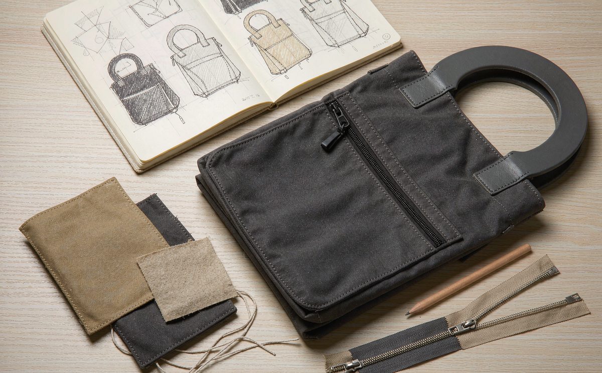 Campaign bag programme plan laid out on a worktable with tech pack sheets, fabric swatches and a sample body