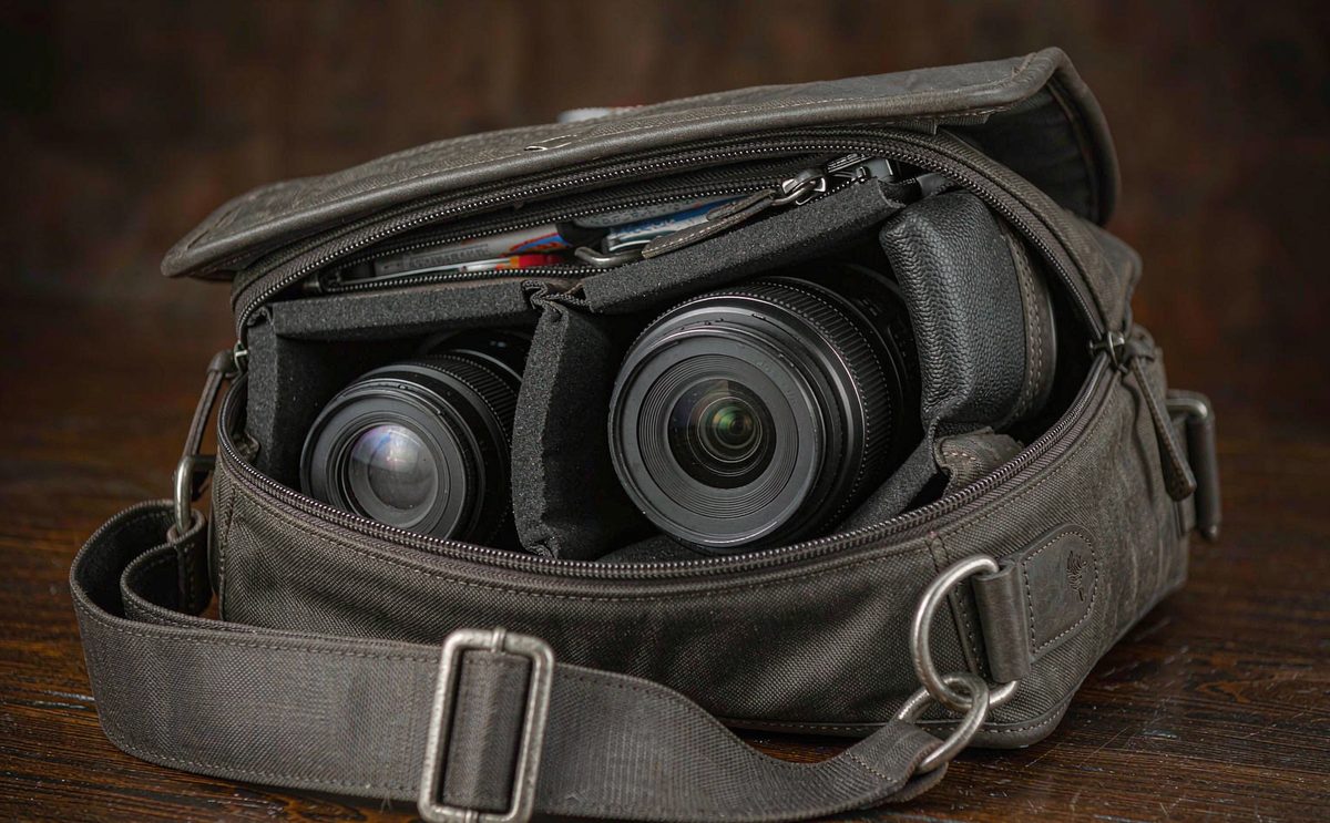 A charcoal camera messenger bag open to show padded dividers and lenses