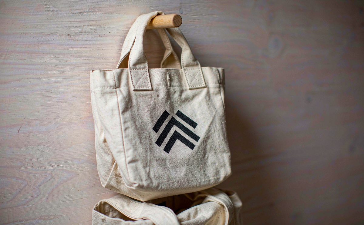 A heavy ecru cotton canvas tote with reinforced handles on a wooden peg