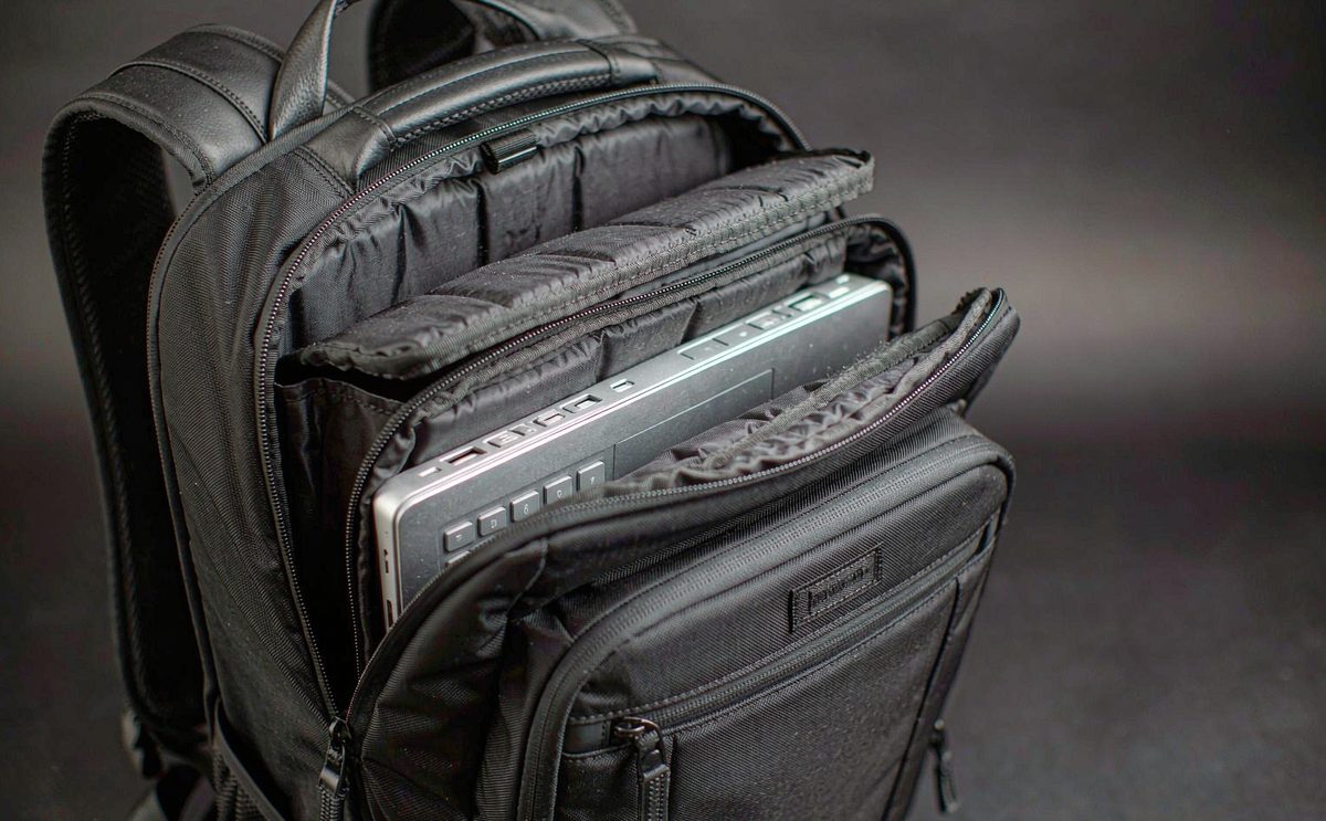 Custom laptop and tech bag prototypes including a padded sleeve, a messenger build and a tech backpack with cable organisers on a sampling bench