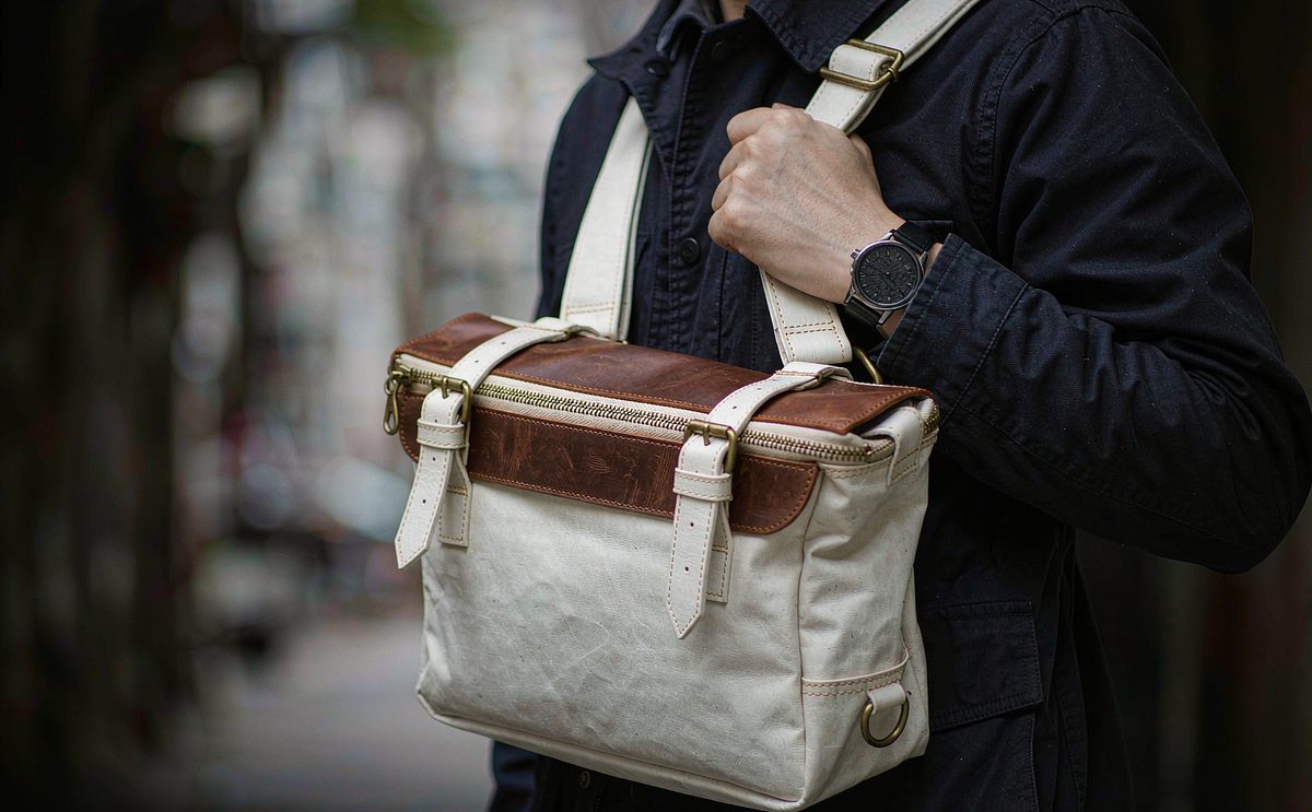 A waxed canvas messenger bag with a leather flap worn across the body