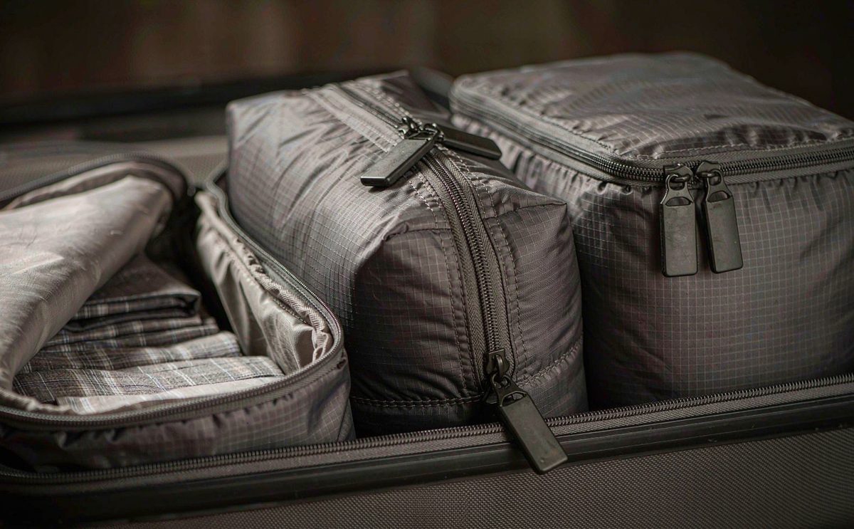 Three grey packing cubes inside an open suitcase, one compressed with a double zip
