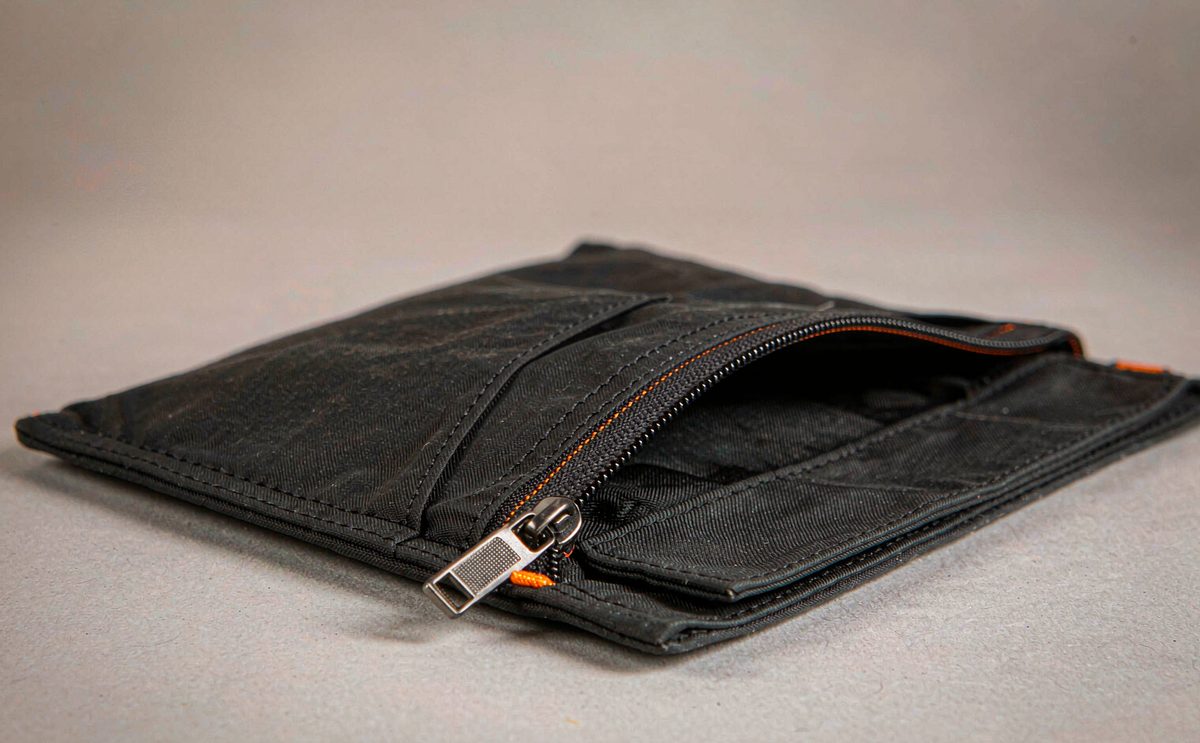 A flat black pouch with contrasting orange zipper tape, half open